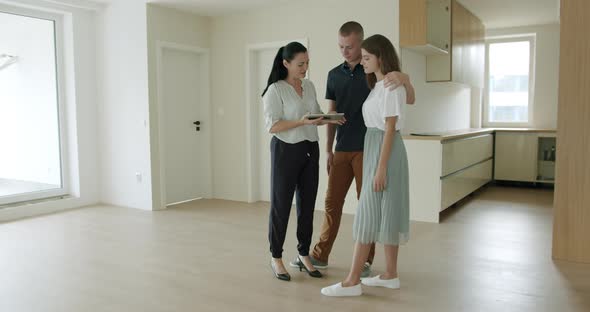 Estate Agent Showing Young Couple Digital Tablet in New Apartment