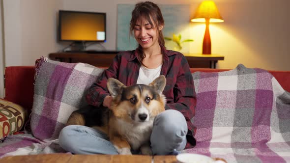 Happy Couple with Cute Pet Welsh Corgi Dog Sitting on Couch at Home at Evening alt
