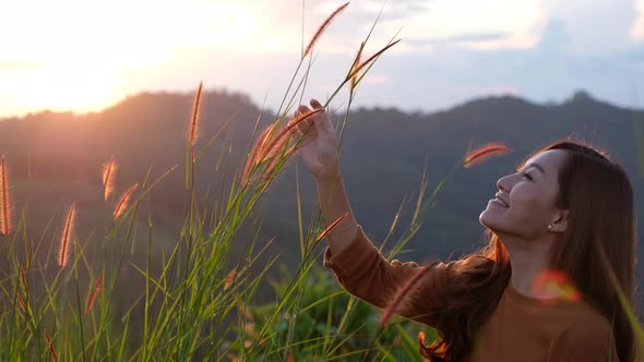 A young woman playing with grass flower with a beautiful mountain views before sunset