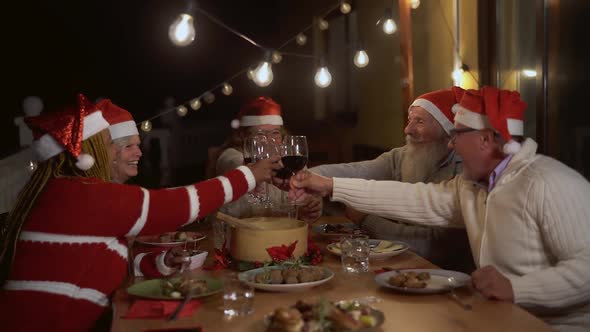 Happy senior friends toasting and celebrating Christmas holidays with red wine glasses alt