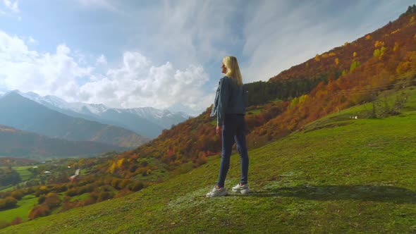 woman in denim jacket is standing on top of mountain, raising her hands in air, alt