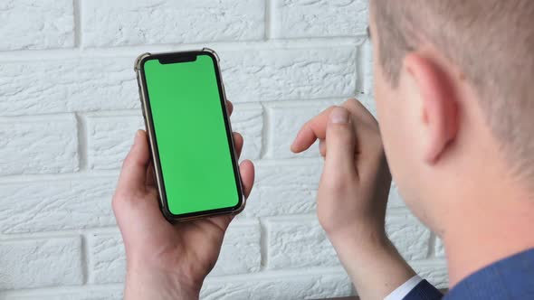 Man Using Smart Phone in Office Space Sitting on Chair and Using Green Screen Phone Mockup Chroma alt