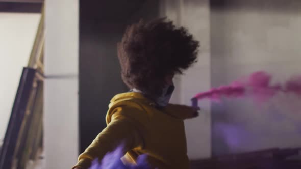 Mixed race woman holding blue and purple flares dancing in an empty building alt