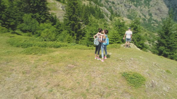 Happy Young Tourists Enjoying the View at the Mountain Summit with Scenic View of Green Valley Below alt