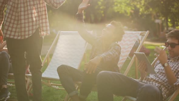 Five Interracial Friends Lying Sitting on Lounges in Park Speaking Smiling Talking in Slowmotion alt