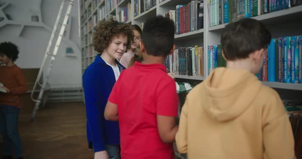 Boy with Kinky Hair Runs to Friend to Choose Book in Library alt