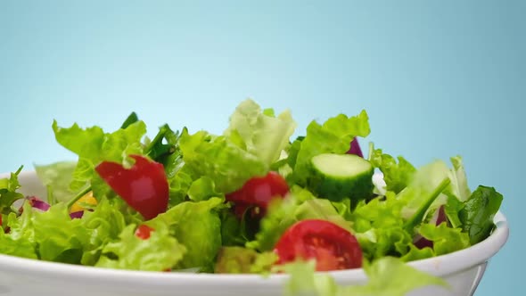 Fresh salad falling in bowl on blue background