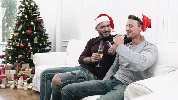 Happy gay male couple celebrating Chritsmas at home sitting on the couch drinking champagne
