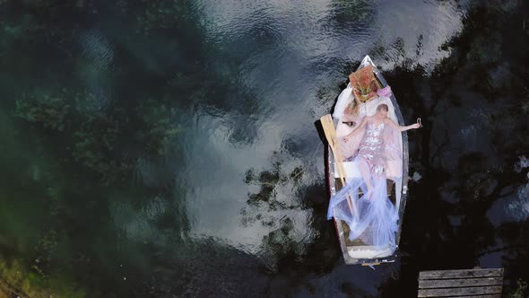 Aerial of fashion influencer on editorial photoshoot laying in rowing boat with picnic in summer, at alt