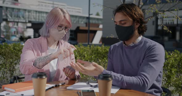 Students Wearing Masks Studying in Street Cafe Spraying Hands with Sanitizer alt