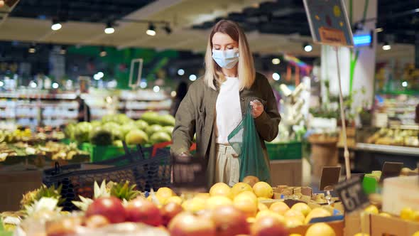 Young woman in face medical protective mask chooses and picks in eco bag vegetables or fruits  alt