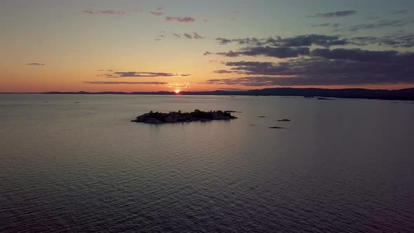 High View of Rocky Pine Tree Island in Blue Lake at Sunset, Drone Aerial Wide Dolly Out. Colorful Cl alt