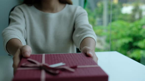 Closeup of a young woman receiving and opening a red present box