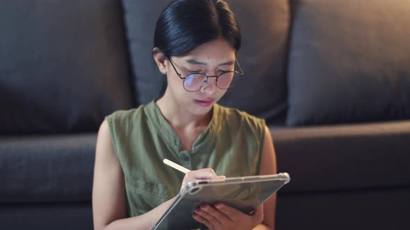 Asian woman wearing glasses writes something on her digital tablet.