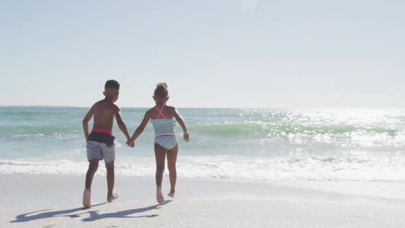 African american siblings running and wearing swimming suits on sunny beach alt