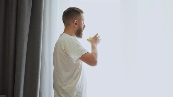 bearded man near the window drinking orange juice. fresh squeezed orange juice alt