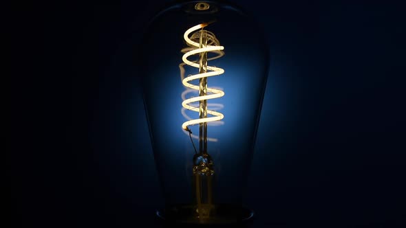 Electric Vintage Edison Light Bulb with a Spiral Flashing on a Blue Background alt