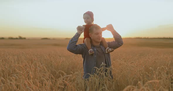 Young Father Walks Across the Field with a Little Girl on His Shoulders