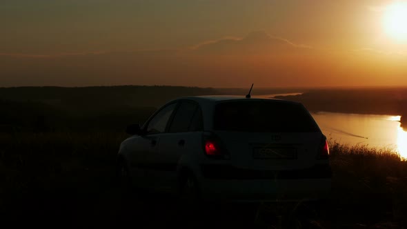 silhouette of couple arriving by car on a cliff overlooking the river at sunset