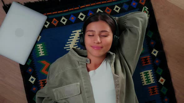 A Young Girl Lies on the Floor Wearing Headphones and Listens to Music with a Smile on Her Face