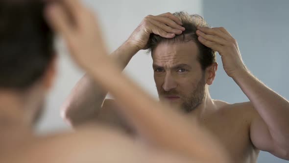 Middle-Aged Man Looking in Mirror at His Bald Patches, Hair Loss Problem alt
