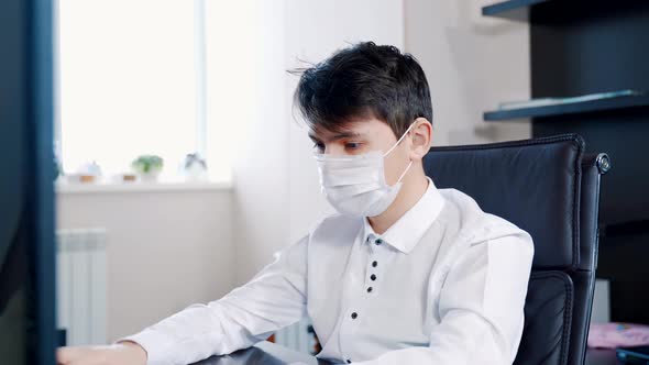 A Young Man in a Medical Mask Performs Homework at a Computer alt