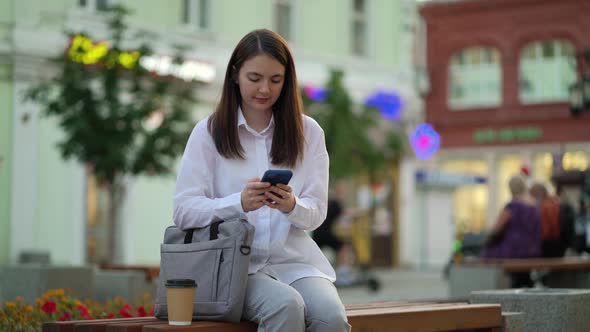 A Lawyer is Sitting on a Bench on a Street in the City Center Typing a Message on His Smartphone alt