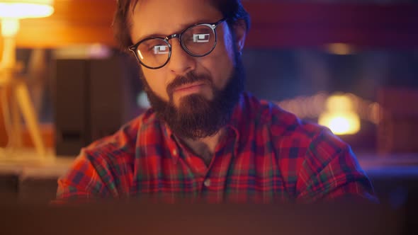Portrait Of a Man Is Working On Laptop Computer With Glasses At Night. Close Up. Businessman Looking alt