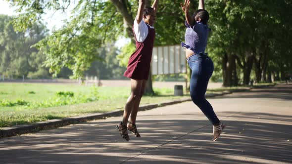 Wide Shot Two Joyful African American Young Women Jumping Up in Slow Motion Laughing alt