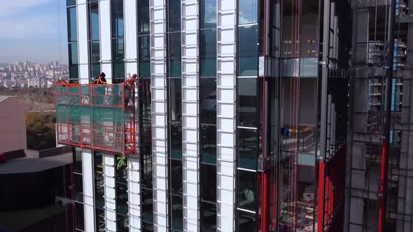 Workers On The Suspended Cradle Are Assembling The Skyscraper Exterior Elements alt