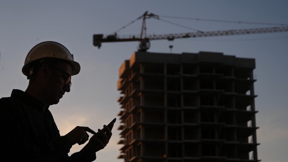 Engineer at the construction site using his phone texting alt