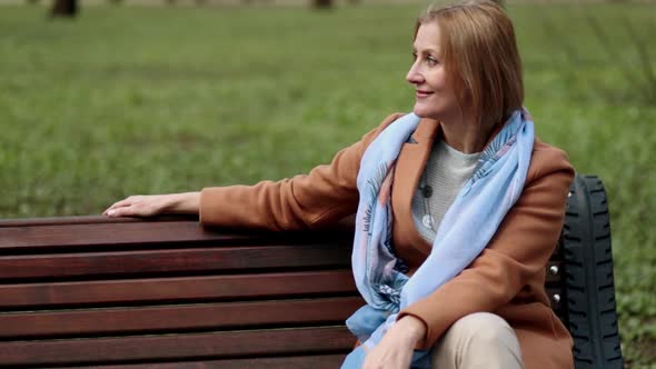 Cheerful Woman Sitting on Bench and Browsing Smartphone