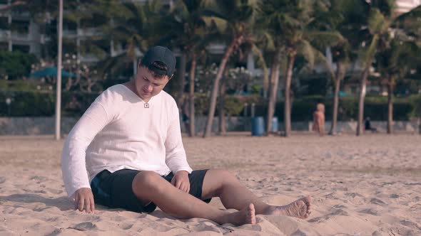 Barefoot Man Plays with Sand on Evening Beach By Ocean alt