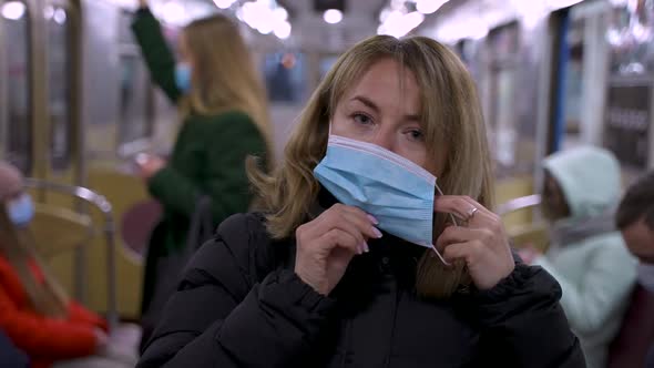 Blonde Woman Putting on Protective Mask in Subway alt