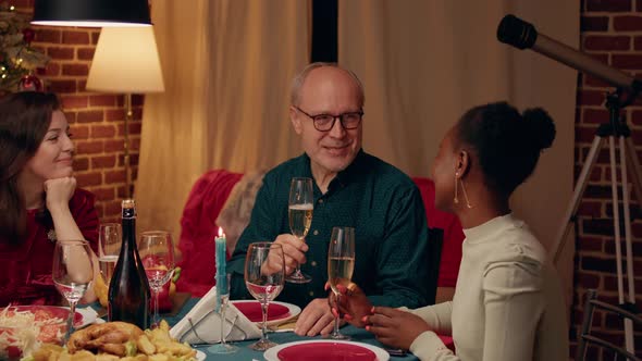 Festive Smiling Senior Man Clinking Glasses with Young Woman at Christmas Dinner Table alt