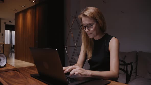 A Woman in a Home Office Sitting at a Table Types Text on a Laptop alt