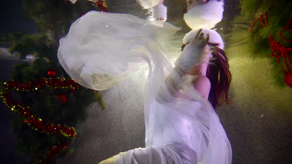 Young Female Model Dressed Like Princess of Winter Is Floating Under Water Near Christmas Tree alt