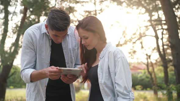 Smiling Loving Happy Couple Standing in Sunbeam in Autumn Forest Talking Surfing Internet on Digital alt