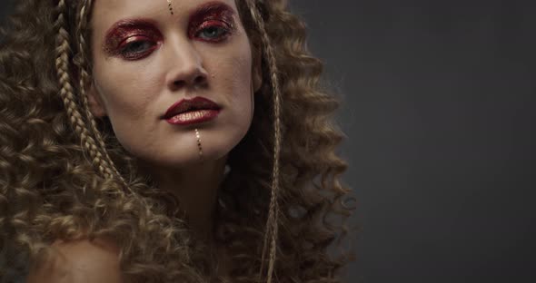 Model in the Studio Is Posing, Wearing Colorful Red and Gold Makeup,  alt