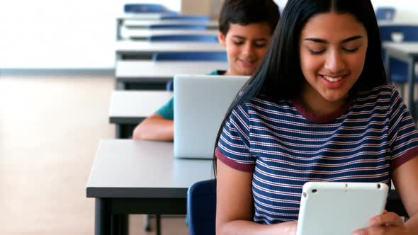 Schoolgirl and schoolboy using laptop and digital tablet while studying in classroom alt