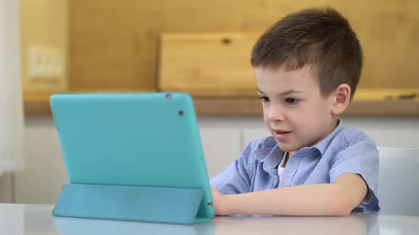 Preschooler Sits at a Table and Looks at a Digital Tablet alt