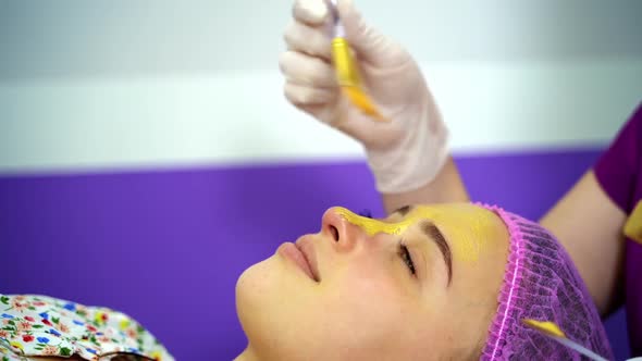 Beautician applies mask to the face of a young woman. Cosmetology.  alt