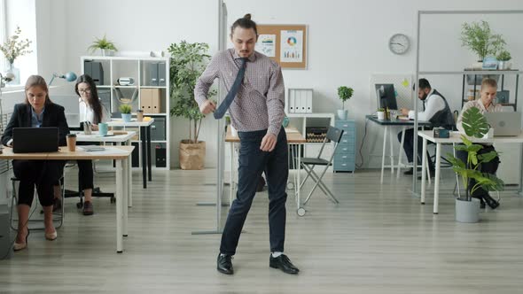 Portrait of Funny Man Dancing in Office While Businesspeople Working in Background alt