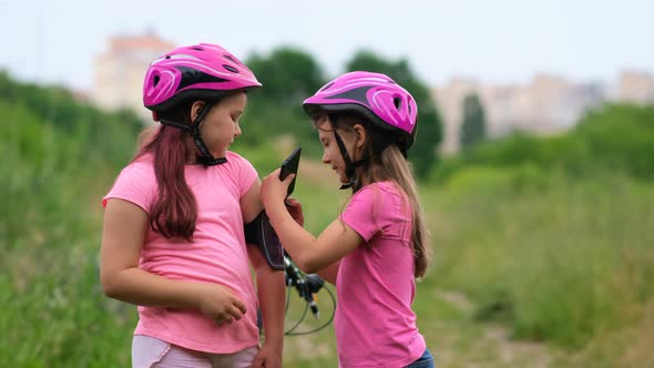 Two girls in pink bicycle helmets and T-shirts take selfies in the park in the summer