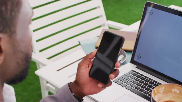 Midsection of african american businessman using smartphone and laptop in cafe alt