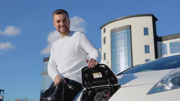 A Fairskinned Male Driver Holds a Charging Cable for an Electric Car alt