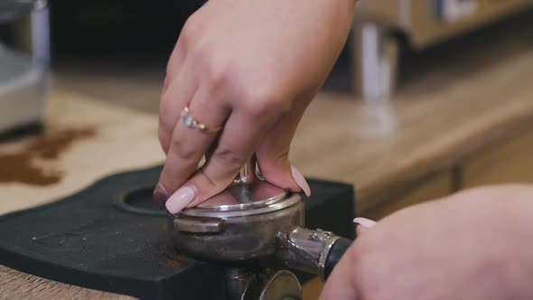 Crop View of Female Barista Pressing Ground Coffee in Portafilter with Tamper on Table