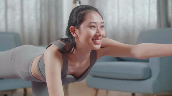 Young Asian Athletic Female In Sports Clothes Doing Yoga In Balancing Table Pose On The Mat At Home alt