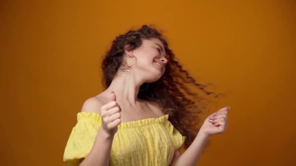 Joyful Young Woman Dancing Against Yellow Background