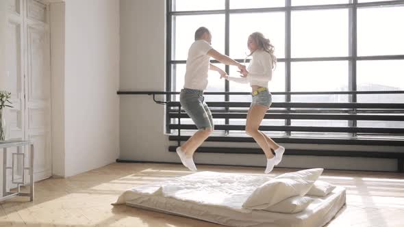 Beloved Are Jumping in Bed Holding Hands in Their New Flat. Relationship Concept.